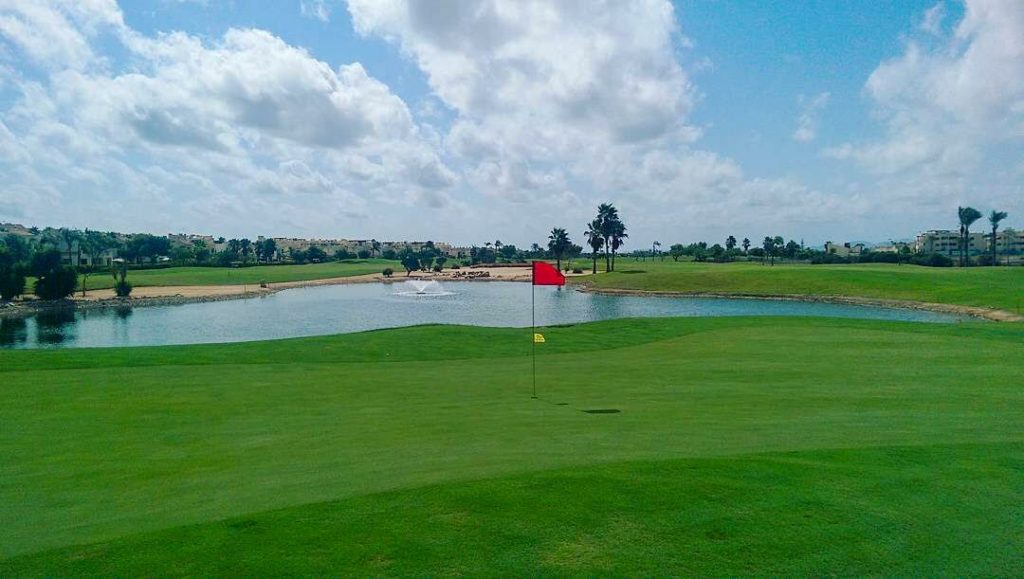 13th green of the Roda Golf Course with water to the right and bunkers left